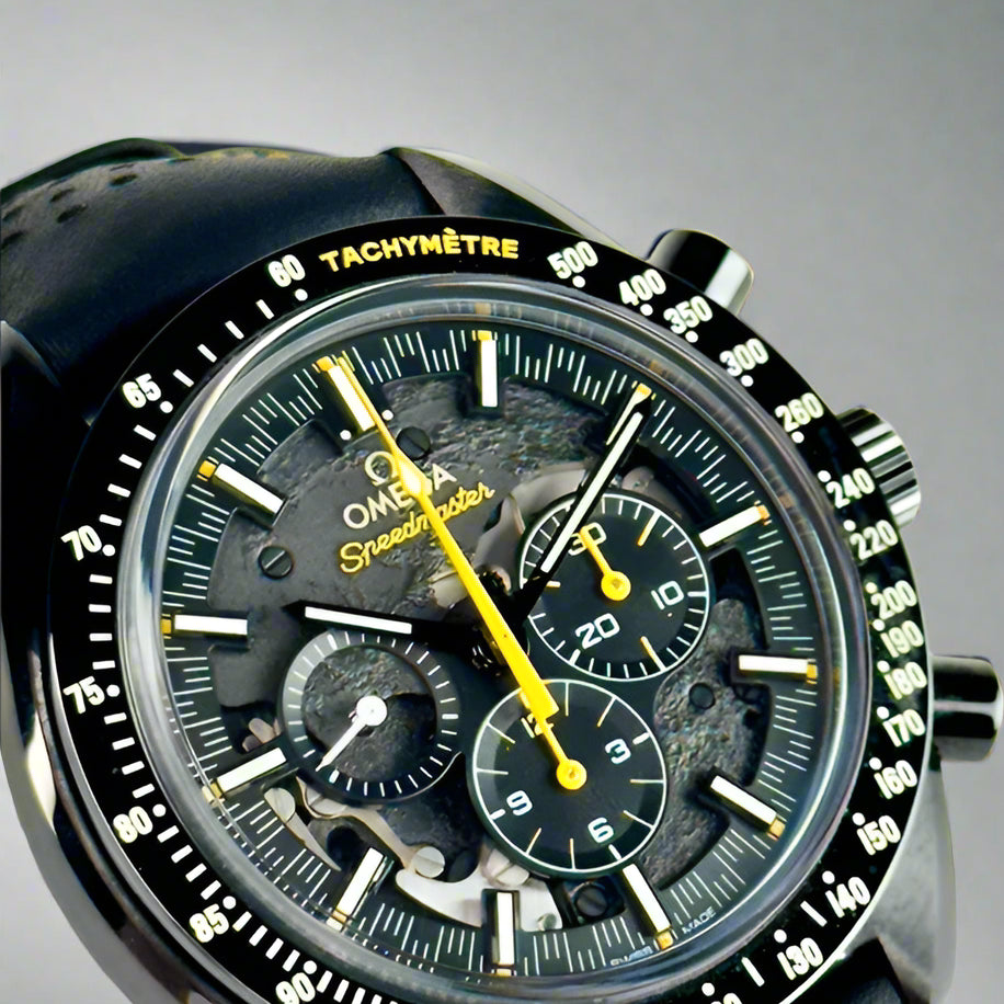 Close-up of a black Omega Speedmaster watch with a detailed face on a light gray background