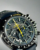 Close-up of a black Omega Speedmaster watch with a detailed face on a light gray background