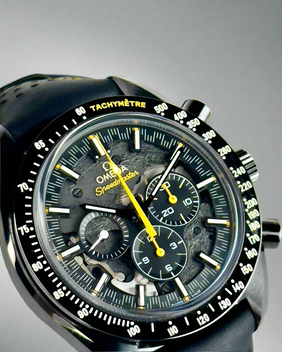 Close-up of a black Omega Speedmaster watch with a detailed face on a light gray background